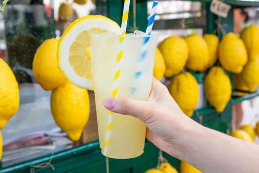 Caucasian hand with healthy fresh lemonade during summer with lemons background