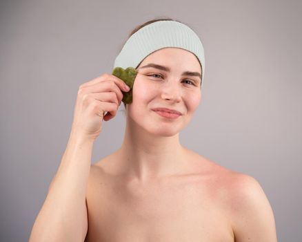 Portrait of a young woman massages her face with a gouache scraper on a white background