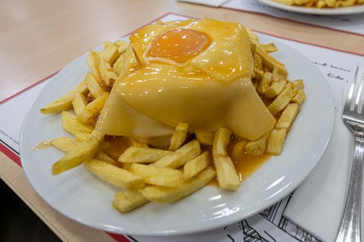 Traditional portuguese sandwich with sauce francesinha on dish.