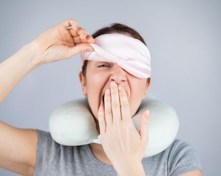 Caucasian woman yawns with travel pillow and sleep mask on white background