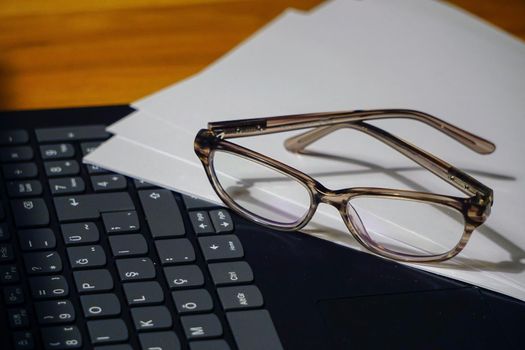 Glasses laptop keyboard and notes on wooden background business concept close up view