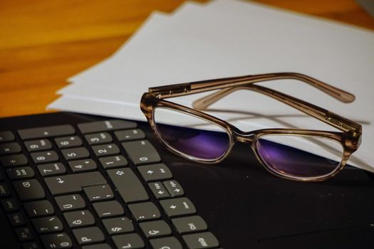 Glasses laptop keyboard and notes on wooden background business concept close up view