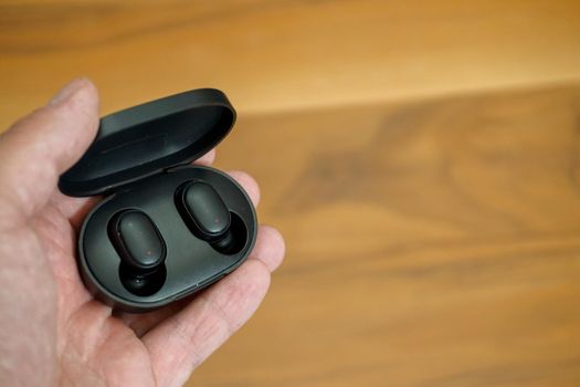 Wireless earphones with charge case in man hand close up view