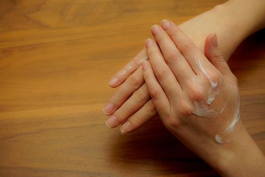 Woman applies hand cream to her hand on wooden isolated background