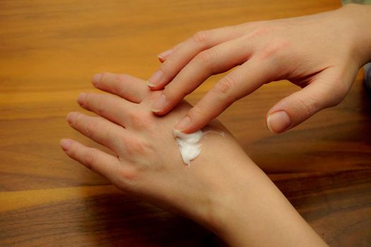 Woman applies hand cream to her hand on wooden isolated background