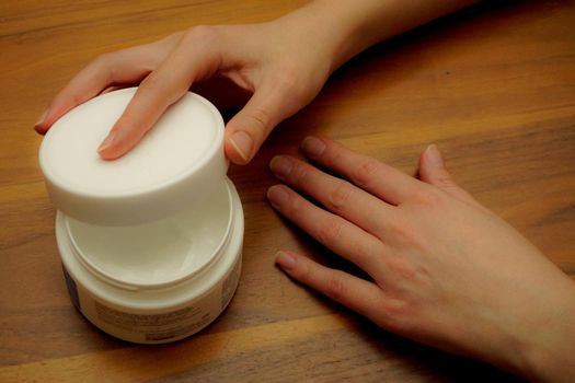 Woman applies hand cream to her hand on wooden isolated background