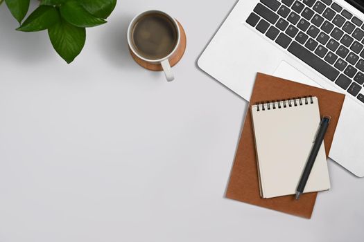 Simple workplace with laptop, notepad, coffee cup and houseplant on white table.