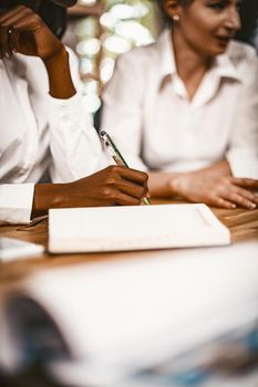 Business Women At Meeting Room, Close Up Of Females Hands, African Woman's hand Holds Pen Writing in Note Pad, Selective Focus On Intelligent Females Hand Making Notes, Toned Image