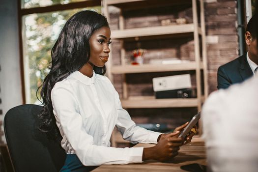 African Business Woman Holds Digital Tablet During Meeting With Coworkers, Young Female Office Manager Smiles Sitting At Table In Meeting Room, Toned Image