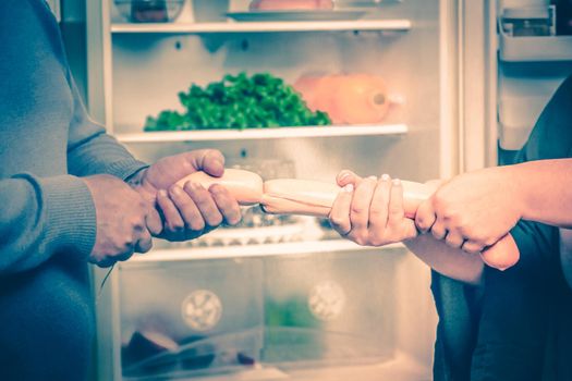 Family Food Competition, Hungry Man And Woman Pull A Sausage Rope While Standing Against The Background Of An Open Refrigerator In Kitchen, Plus Size Husband And Wife Are Fighting For Sausages