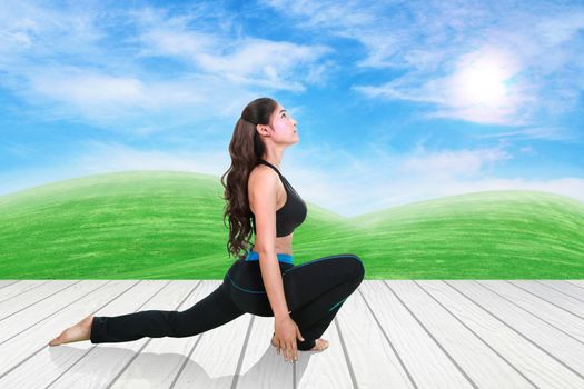 Young woman doing yoga exercise on wood floor with green grass and sky