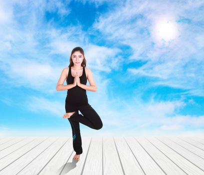 Young woman doing yoga exercise on wood floor with sky