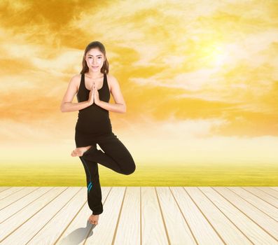 Young woman doing yoga exercise on wood floor with field at sunset