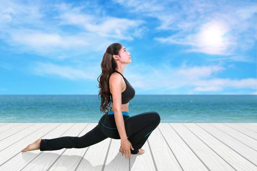 Young woman doing yoga exercise on wood floor with sea and sky