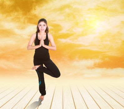 Young woman doing yoga exercise on wood floor at sunset