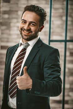 Thumb Up Gesture From Toothy Smiling Businessman In Office, Positive Caucasian Man In Elegance Formalwear Stands On Wall Background, Toned Image