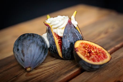 Fresh sliced purple figs with whipped cream on a wooden background from old boards. Raw exotic figs. Low key