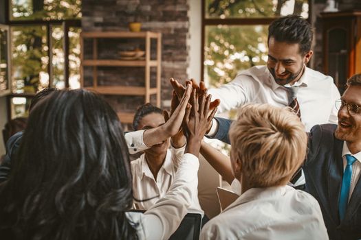 Business Group Of Colleagues Joined Hands While Sitting At Table In Office, High Five Gesture From Male And Female Team, Corporate Team Building Concept, Toned Image