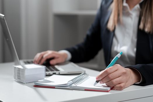 Businesswoman Writing In Notebook And Typing On Lap Top Od Desk With Notes.