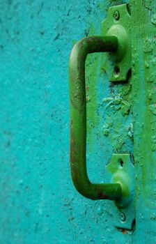 An old doorknob covered in uneven green paint. Old vintage wooden door with handle