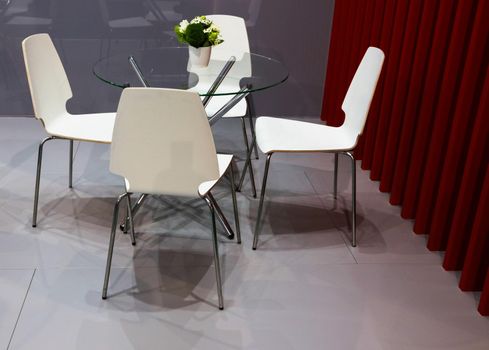 White chairs and a round glass table, a vase with a bouquet of flowers and a red wall.