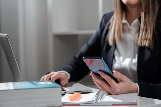 Businesswoman Holding Mobile Phone And Typing On Lap Top On Desk.