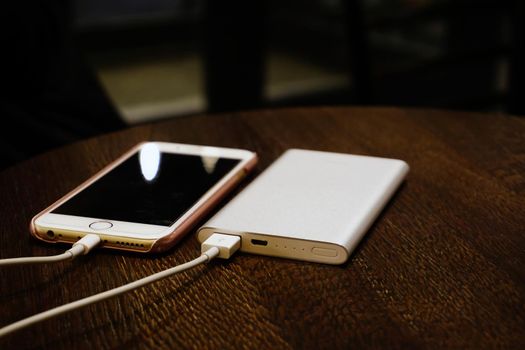 Powerbank charging smartphone on wooden background close up view