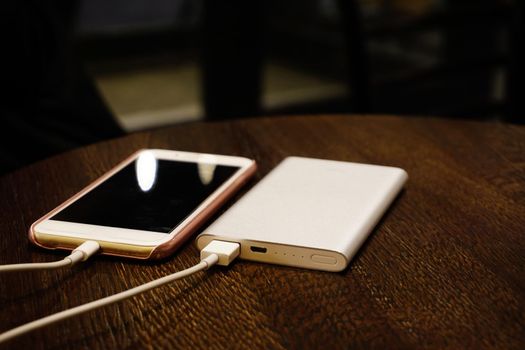Powerbank charging smartphone close up view on wooden background