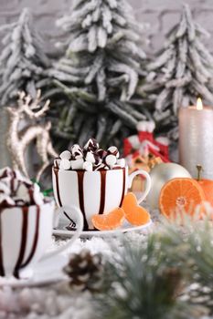 Hot chocolate with marshmallows in a white ceramic mug, with tangerines on a snowy table. The concept of a cozy holiday for Christmas and New Year.