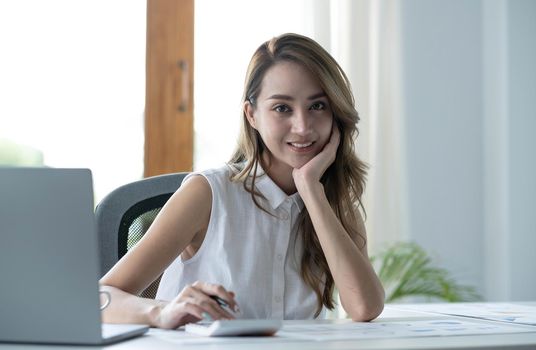 Charming Asian woman working at the office using a laptop Looking at the camera..