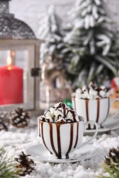 Hot chocolate with marshmallows in a white ceramic mug, with tangerines on a snowy table. The concept of a cozy holiday for Christmas and New Year.