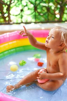 Little girl sits in an inflatable pool on the balcony with a toy in her hand. High quality photo