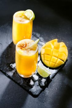 Two Mangonada summer cocktails on a dark background with ice and lime slices. Top view.