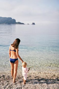 Mom stands with a little girl on the beach. High quality photo