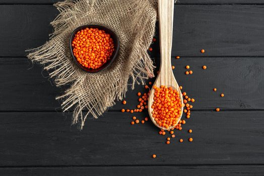 Red lentils on a rustic dark wooden background. Cereal lentils on a wooden spoon. Ancient grain food. Dry orange lentil grains, heap of dal, raw daal, dhal, masoor, Lens culinaris or Lens esculenta