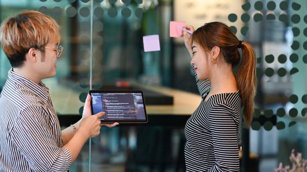 Young male software developer holding digital tablet, discussing online project with his colleagues at creative office.