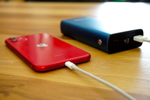 30 April 2021 Eskisehir Turkey. Red iphone 11 being charged by powerbank on wooden table