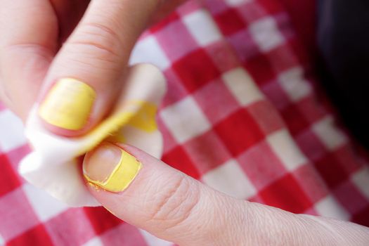 Woman removing nail polish on red table cloth background close up view