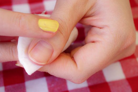 Woman removing nail polish on red table cloth background close up view