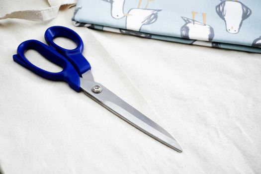 White fabric and blue scissor on isolated background close up view