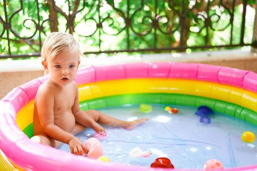 Little girl sits in an inflatable pool on the balcony. High quality photo