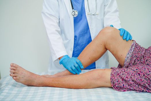 Doctor checking Asian elderly woman patient with scar knee replacement surgery in hospital.