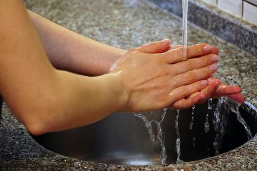 Woman washing hands with water and soap under the water in the kitchen