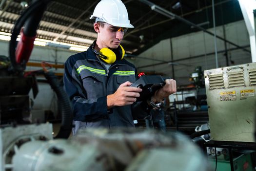 Young factory worker working with adept robotic arm in a workshop . Industry robot programming software for automated manufacturing technology .