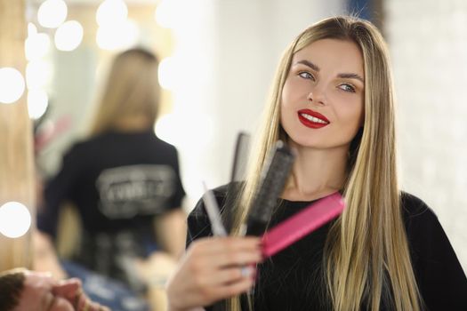 Happy young girl hairdresser holding different combs, close-up. Beauty salon stylist woman, profession