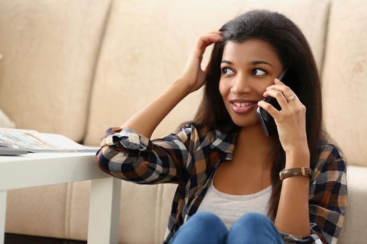 A dark-skinned girl on the floor of the house speaks on a smartphone, close-up. Surprised teenager pondering