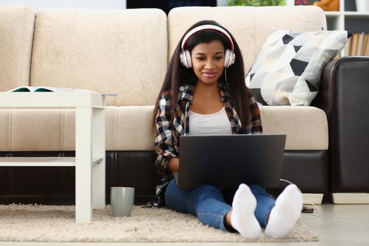 A dark-skinned girl in headphones with a laptop sits on the floor, close-up. Homeschooling student during quarantine