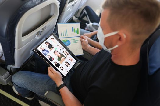 A man in a protective mask with a tablet and documents on the plane, close-up. Teamwork, report chart