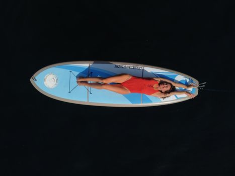 Young attractive brunette woman in red swimsuit, swimming on kayak around volcanic rocks, like in Iceland. Back view. Christmas holiday vacation and travel concept.