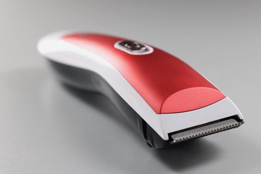 Close-up of electric trimming machine for hair, device with red colour design on grey surface. Equipment to create hairstyle. Hairdresser, barber concept